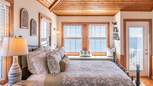 A bedroom with a bed, a nightstand, a lamp, and a window with a view. - Unbeatable Views & Coastal Charm (Harkers Island)