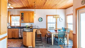 A kitchen with wooden cabinets, a central island, bar stools, and a dining table with chairs. - Unbeatable Views & Coastal Charm (Harkers Island)