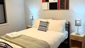 A neatly made bed with a patterned pillow, a bedside lamp, and a small wooden nightstand.