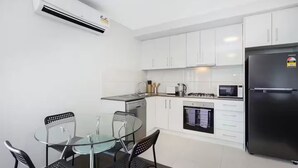 A modern kitchen with white cabinets, a black refrigerator, a glass dining table with four chairs, and an oven.