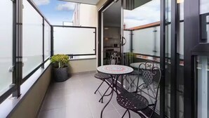 A balcony with a glass door, a small round table with chairs, and a potted plant.