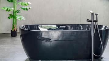 Una bañera independiente negra en un baño moderno, con una planta en maceta y un perchero de toallas en la pared.