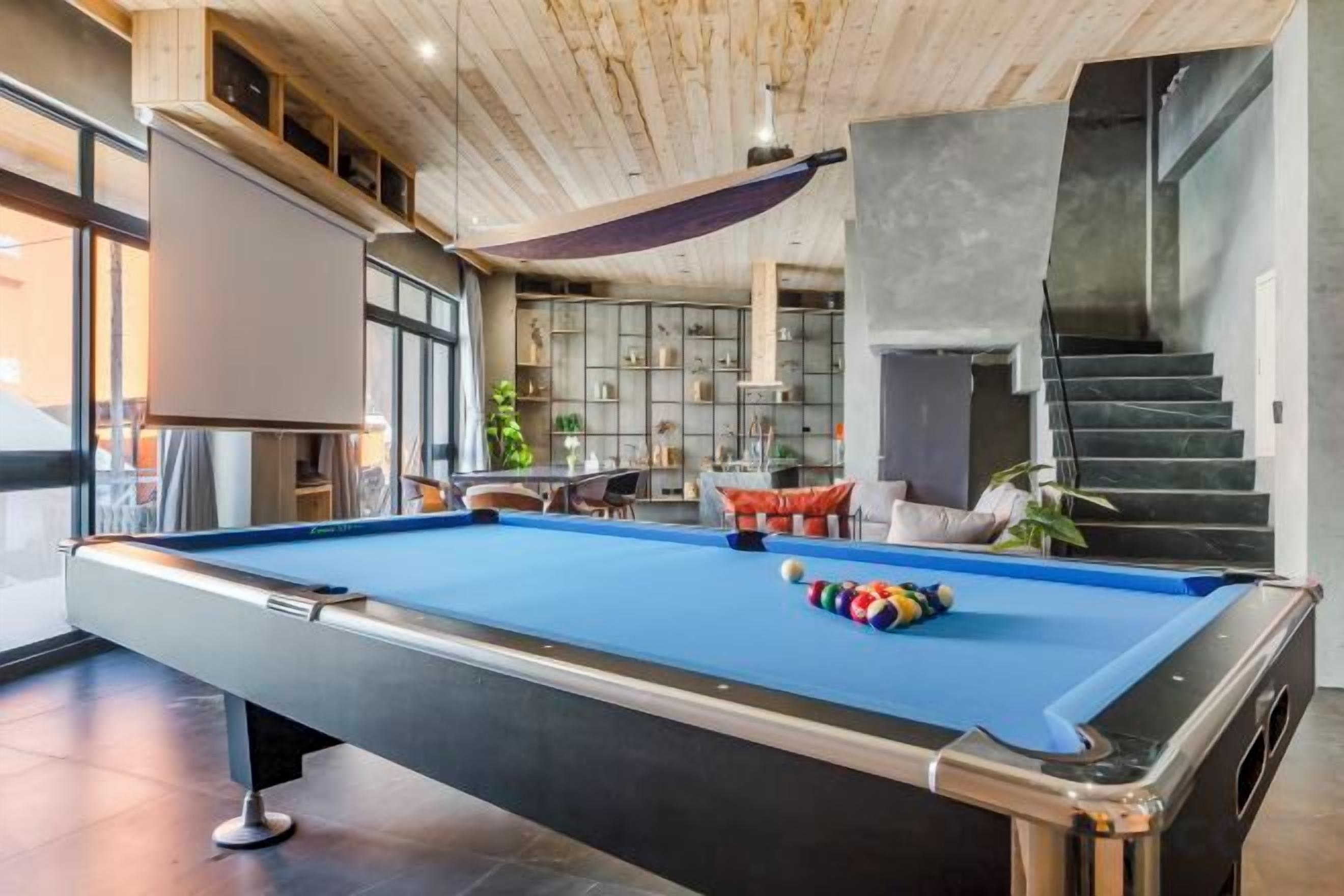 A pool table in a modern room with a staircase and seating area.
