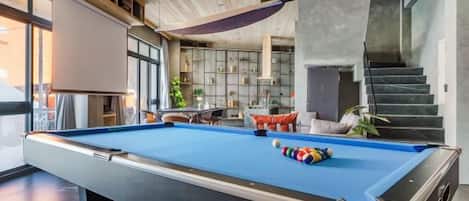 A pool table in a modern room with a staircase and seating area.