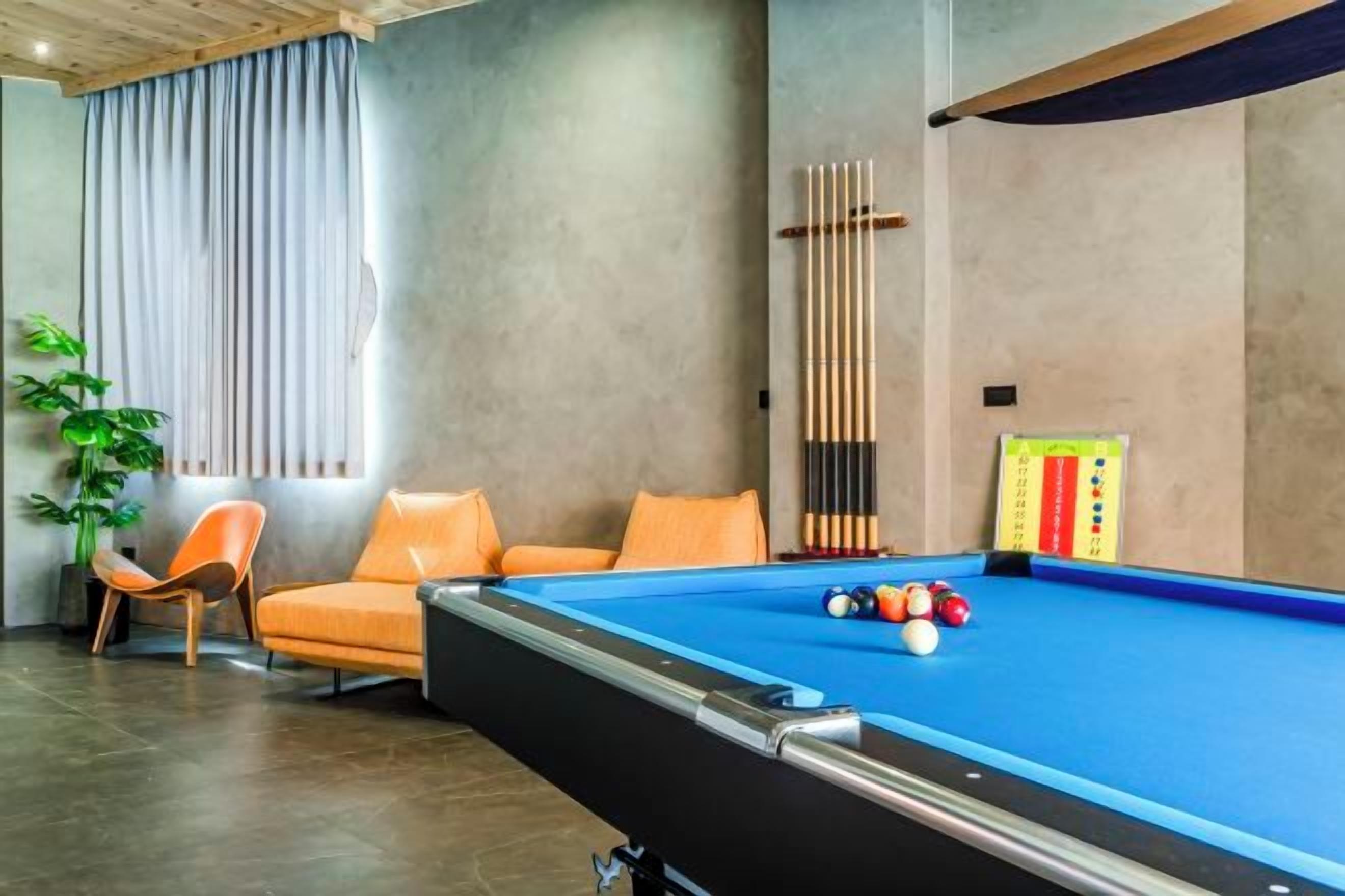 A pool table with balls, a pool cue, and a billiards scoreboard in a room with a modern design, including a plant and a chair.