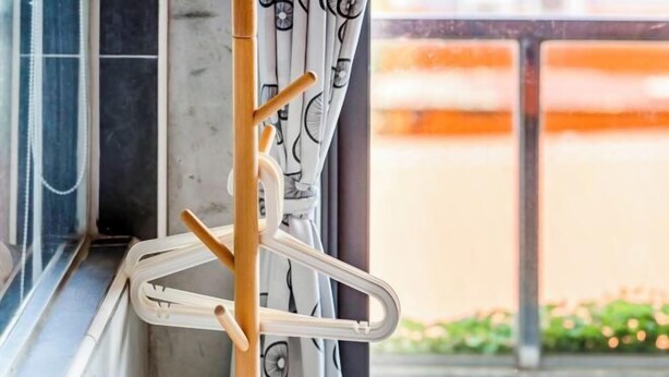 A window with a wooden rack holding a white hanger, a window blind with a pattern, and a view of a building outside. - Harajuku Inn (Pingtung)