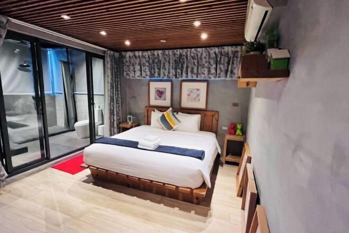 Una camera da letto con un letto, un tappetino rosso, una testiera in legno, un comodino e un condizionatore d'aria a parete.