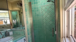 A bathroom with a glass shower enclosure, a sink with a mirror, and a tiled floor. - The Sweet Spot SB (Santa Barbara)