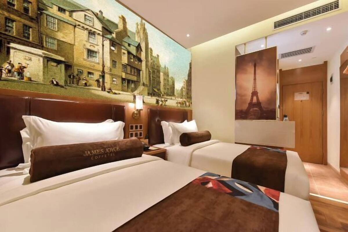 Een hotelkamer met twee bedden, een grote muurschildering van een stadsgezicht en een poster van de Eiffeltoren.