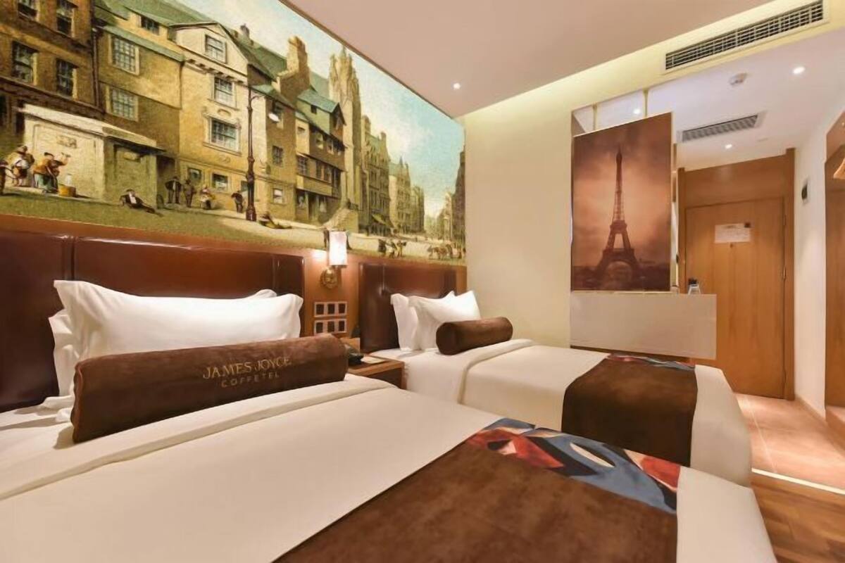 Hotelkamer met twee bedden, een muurschildering van een stadsgezicht, een poster van de Eiffeltoren en een bordje op de deur.