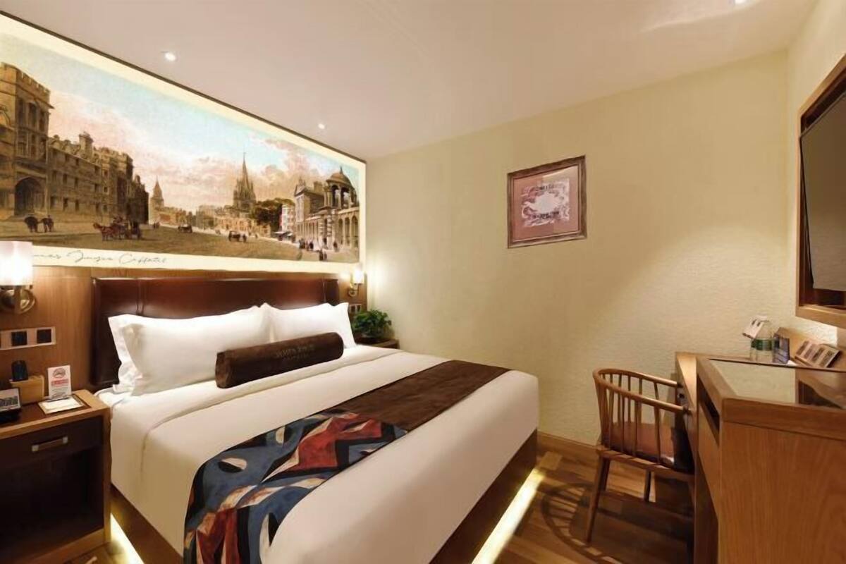 Een hotelkamer met een groot bed, een bureau en een stoel. Er hangt een schilderij aan de muur en een lijst met een foto boven het bed.