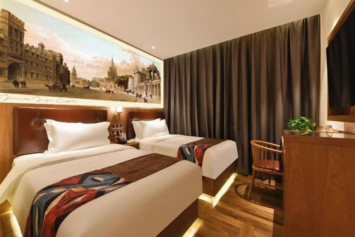 Een hotelkamer met twee bedden, een houten hoofdbord, een bureau, een stoel en een groot schilderij aan de muur.