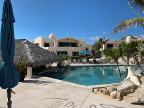 A swimming pool with lounge chairs, a thatched-roof structure, and a building with a dome.