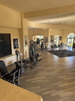 Ein Fitnessstudio mit verschiedenen Trainingsgeräten, Holzboden und motivierenden Postern an den Wänden.