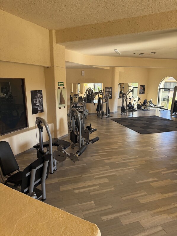 Une salle de sport équipée de divers appareils d’exercice, dotée d’un plancher en bois et ornée d’affiches motivantes.