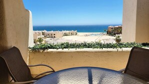 A balcony with a view of a beach and ocean, featuring a table and chairs.