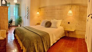 A cozy bedroom with a wooden headboard, a bed with white linens, a bench, and a potted plant. - Chateau du rey Restaurant L'Abeuradou (Saint-Andre-de-Majencoules)