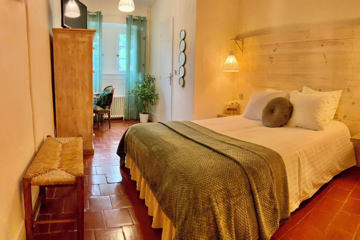Une chambre à coucher accueillante, avec une tête de lit en bois, un lit recouvert de draps blancs, un banc et une plante en pot.