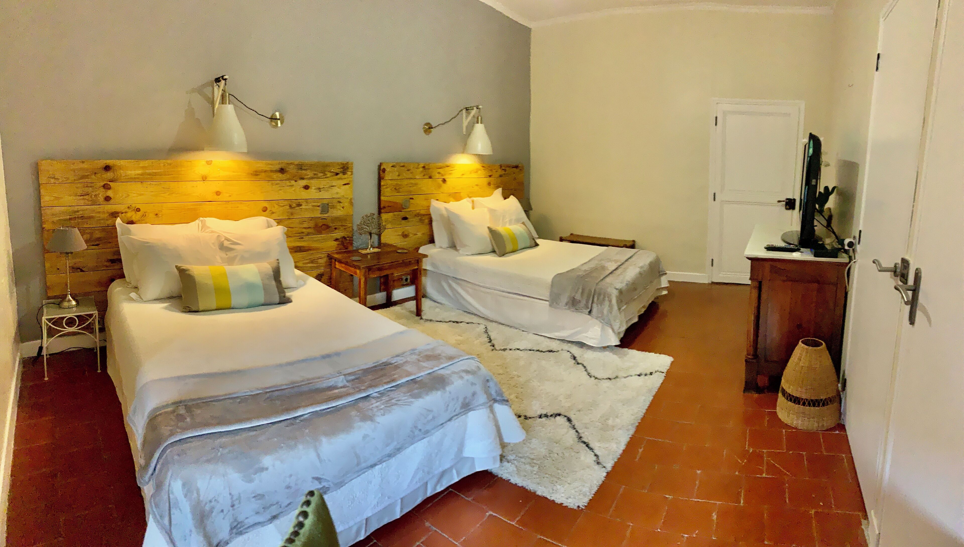 A room with two beds, wooden headboards, bedside lamps, a small table, and a door.