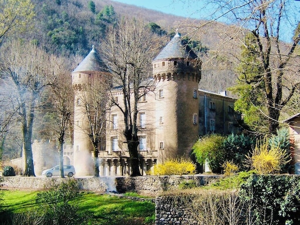 Un castillo con dos torres, rodeado de árboles y un muro de piedra.