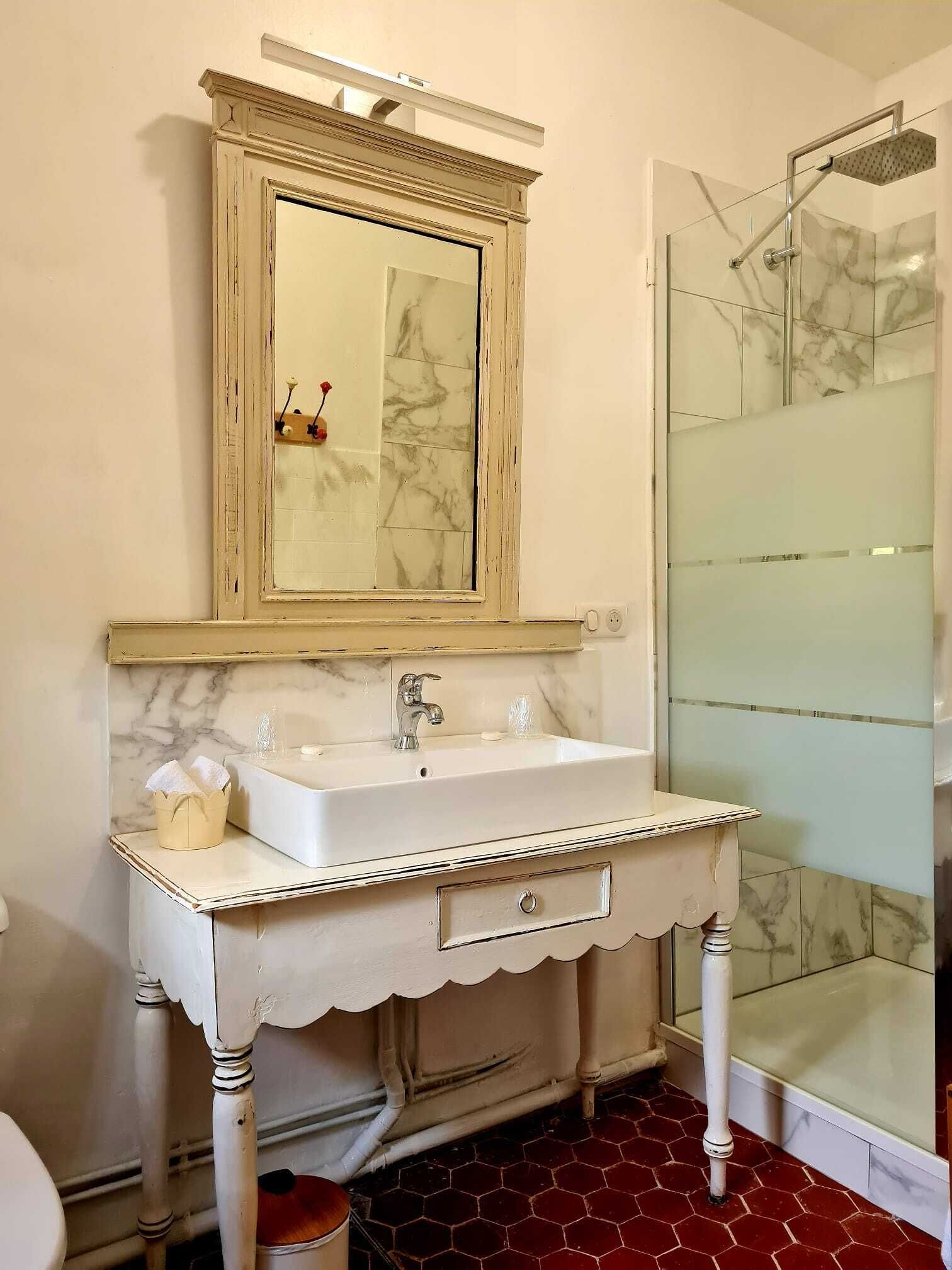 A bathroom with a white vanity, a mirror, a sink, and a shower area.