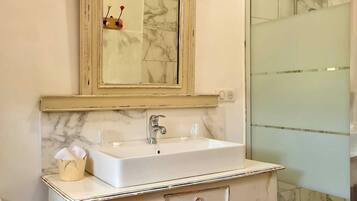 A bathroom with a white vanity, a mirror, a sink, and a shower area.