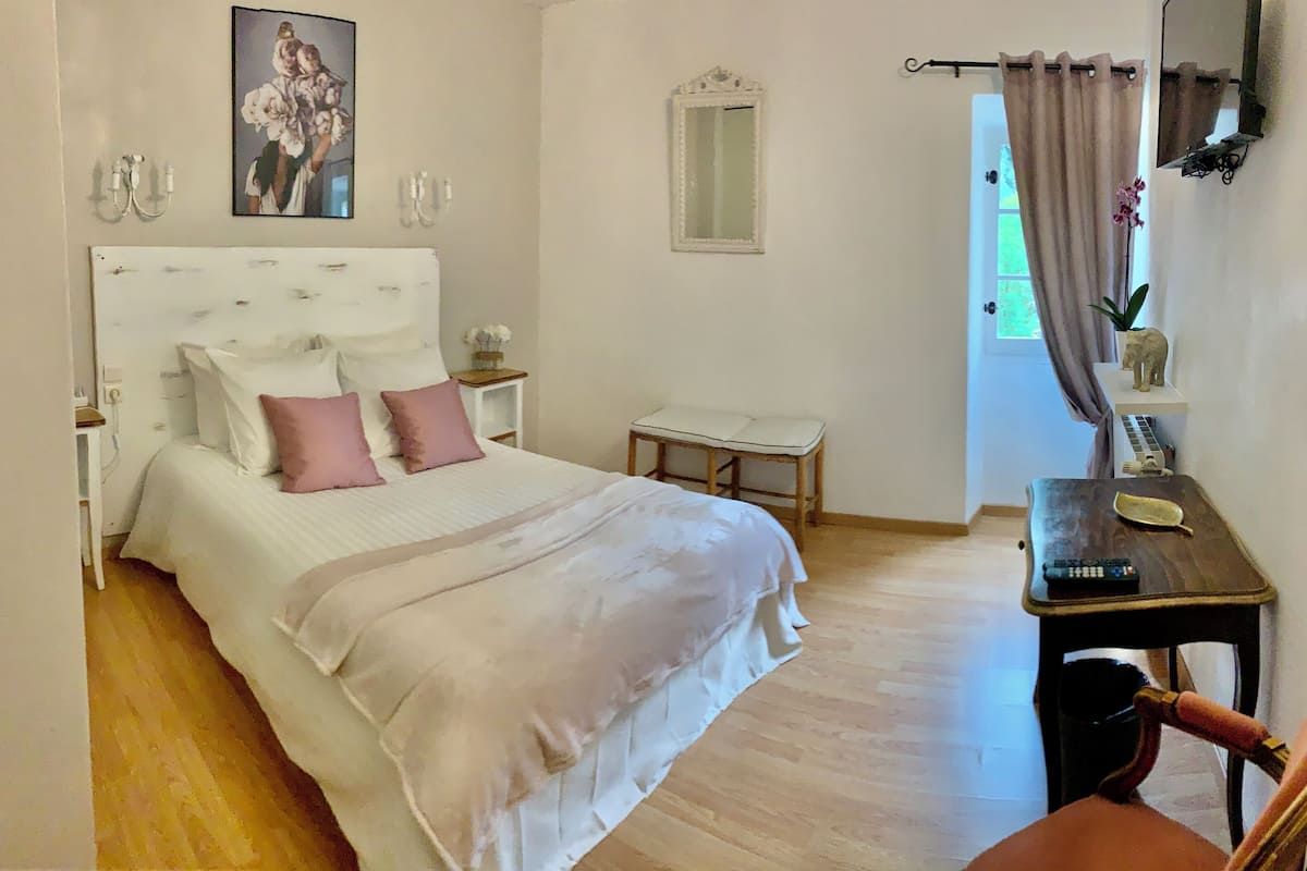 Une chambre à coucher comprenant un lit, des tables de chevet, un miroir, une petite table avec une chaise et une fenêtre avec des rideaux.