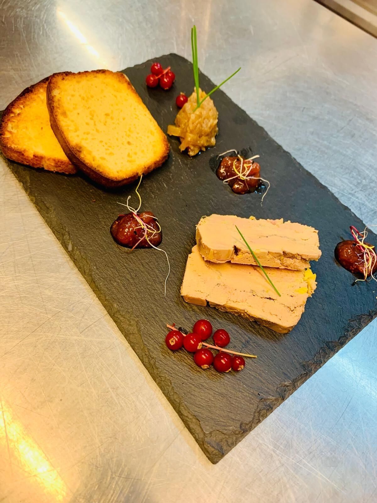 Een grijze serveerplank met sneetjes brood, een stukje paté en garnering met rode bessen en bies.