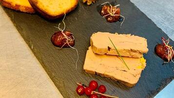 Een grijze serveerplank met sneetjes brood, een stukje paté en garnering met rode bessen en bies.
