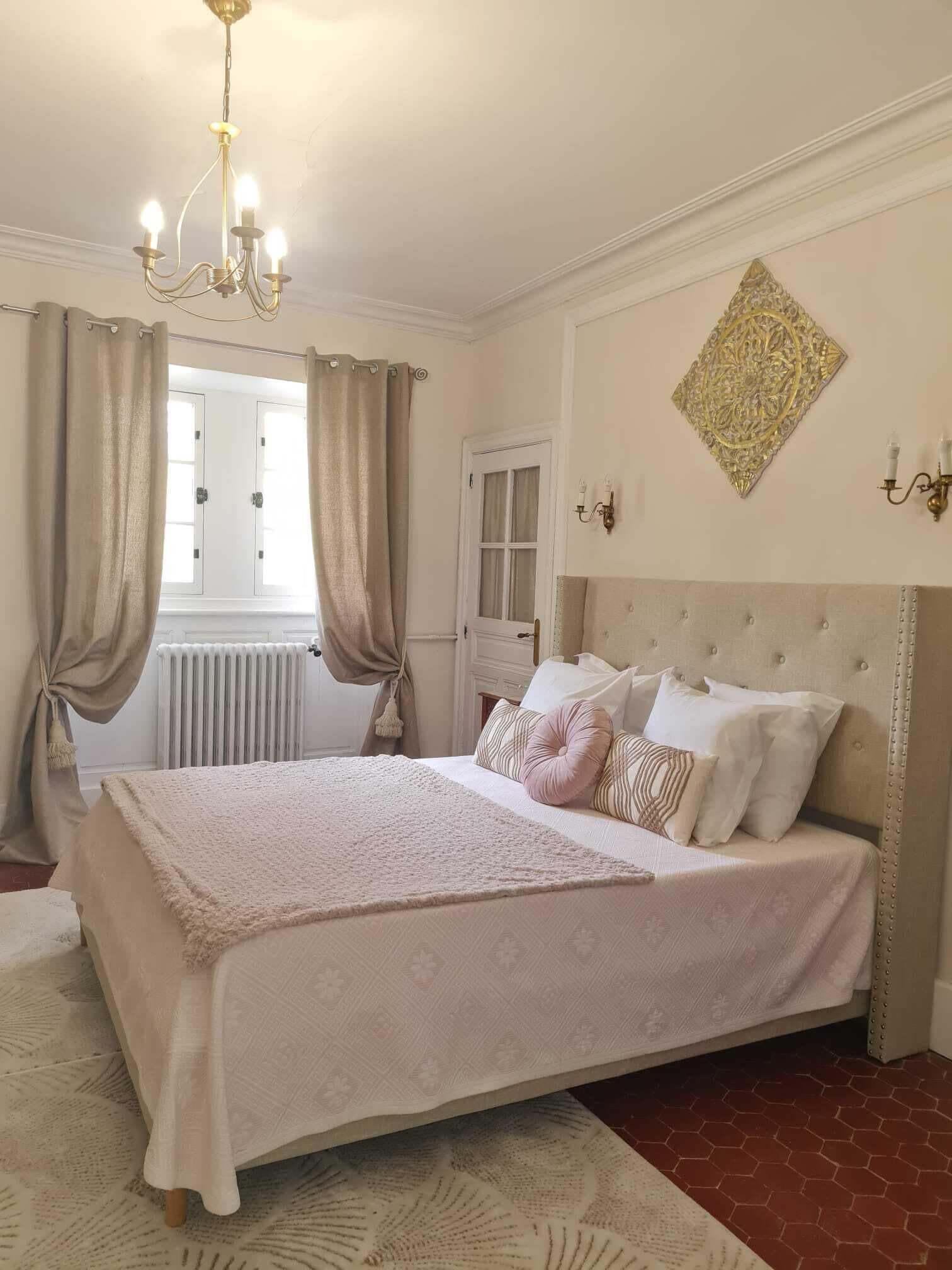 Ein Schlafzimmer mit einem großen Bett, einer Chandelier, einem Heizkörper und einem Fenster mit Vorhängen.