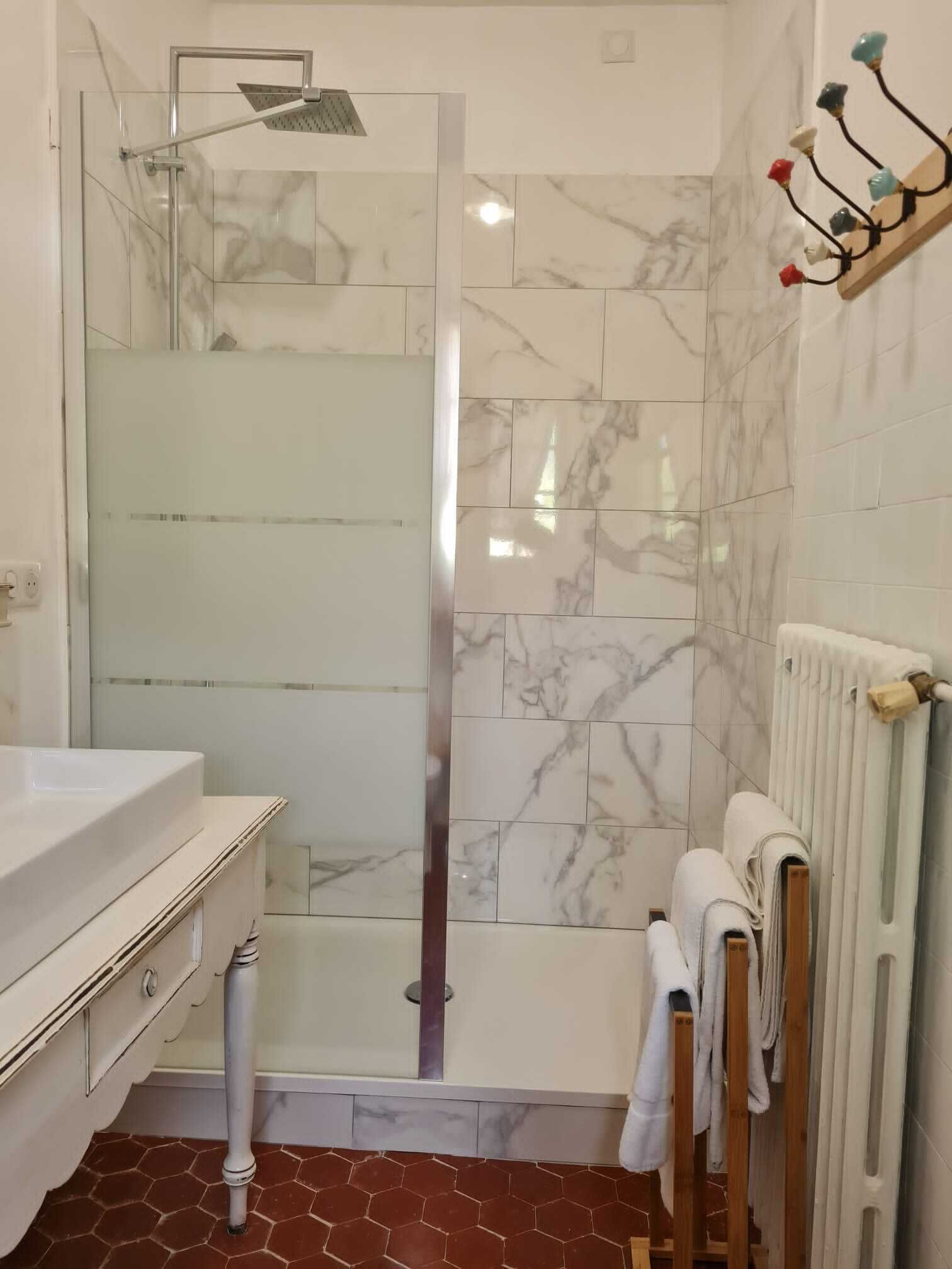 A bathroom with a glass shower enclosure, a white sink, and a towel rack with towels.