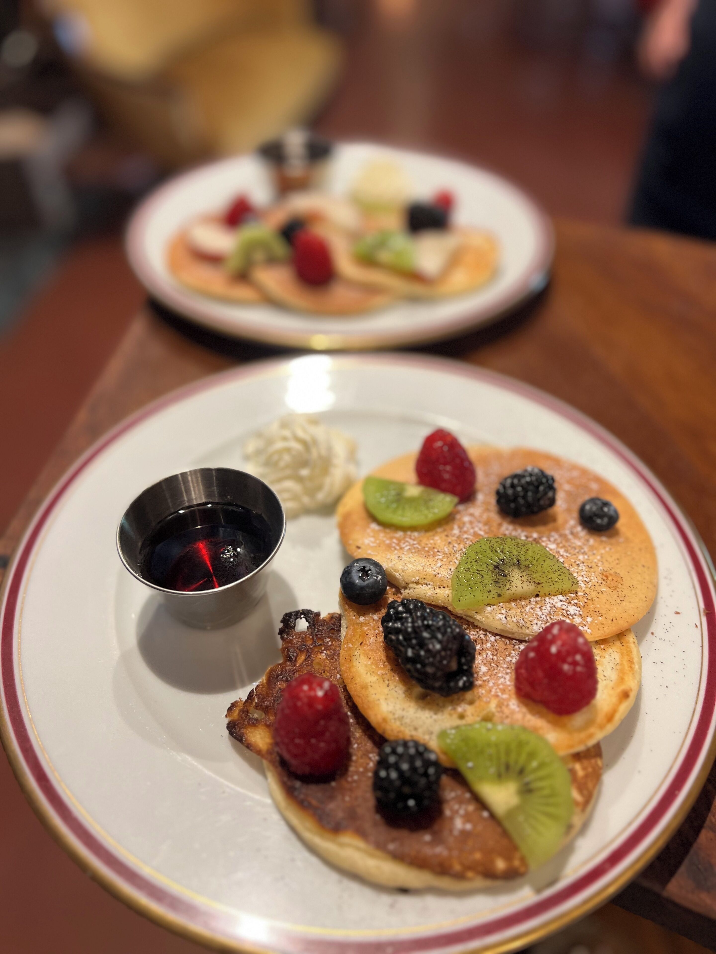 Desayuno con tortitas cubiertas de frutos rojos y una taza pequeña de jarabe.