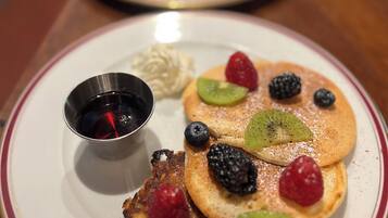 Desayuno con tortitas cubiertas de frutos rojos y una taza pequeña de jarabe.