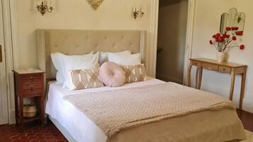 A bedroom with a large bed, a chandelier, a decorative wall piece, and a small table with a vase.