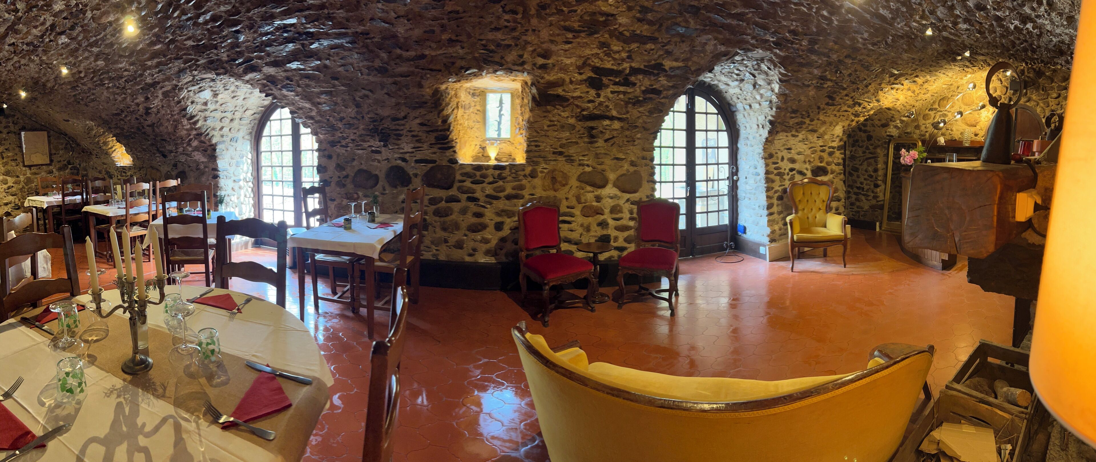 A rustic dining area with stone walls, wooden tables, and red chairs.