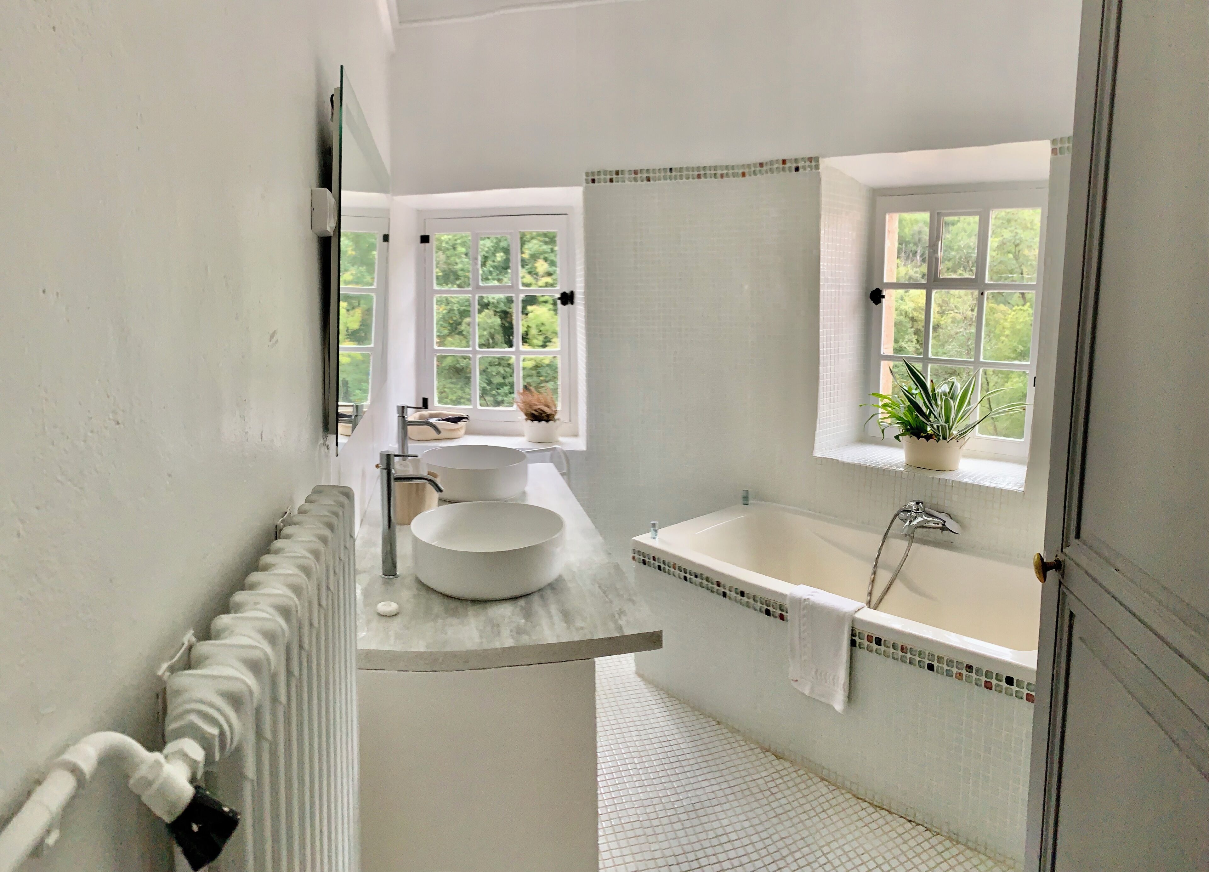 A modern bathroom with a large bathtub, a round sink, and a window providing a view of greenery.