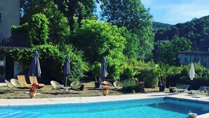 A swimming pool with lounge chairs and umbrellas, surrounded by lush greenery and trees. - Chateau du rey Restaurant L'Abeuradou (Saint-Andre-de-Majencoules)
