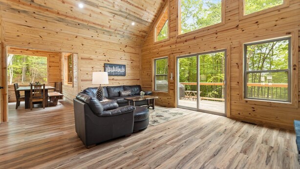 A spacious wooden cabin interior with a large leather sofa, dining table, and chairs. - Rustic Retreat with Modern Comforts (Zoe)