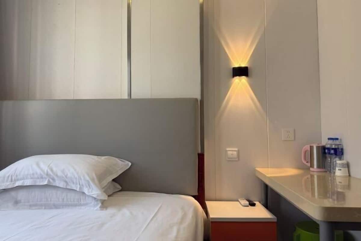 Une chambre d’hôtel comprenant un lit, une table de chevet, une lampe fixée au mur et une petite table sur laquelle se trouvent une télécommande et une bouteille d’eau.