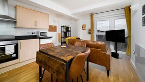Una cocina moderna con armarios de madera, una mesa de comedor con sillas, un televisor y vistas de la ciudad a través de un ventanal amplio.