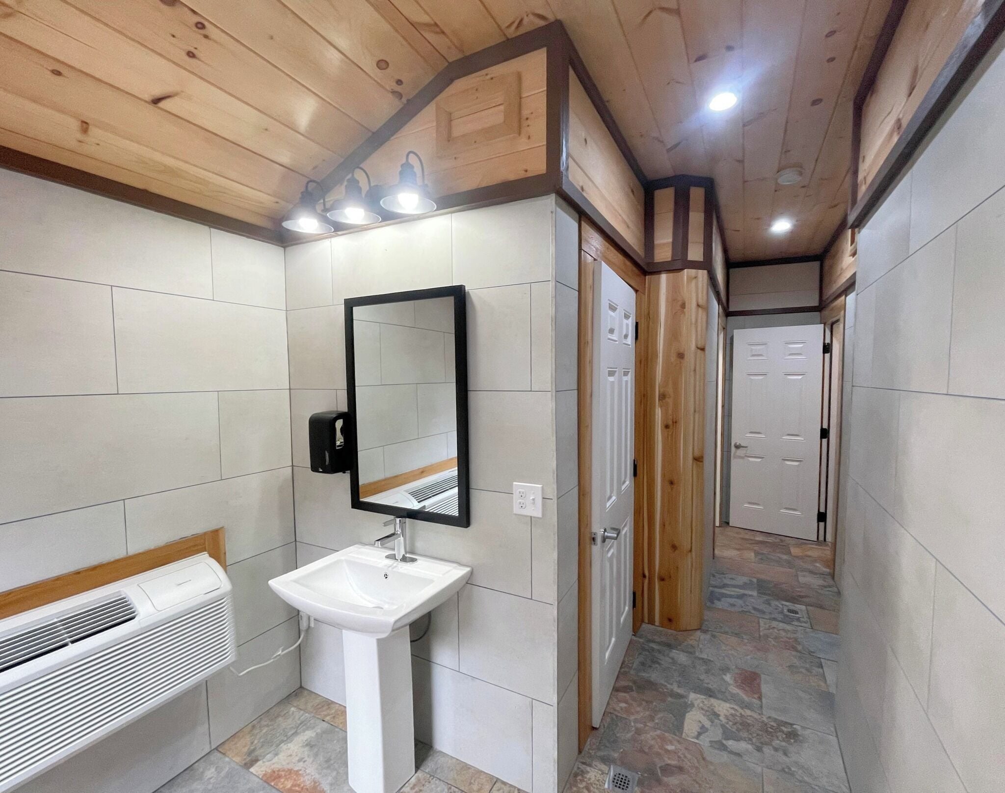 A bathroom with a white sink, mirror, and wooden ceiling.
