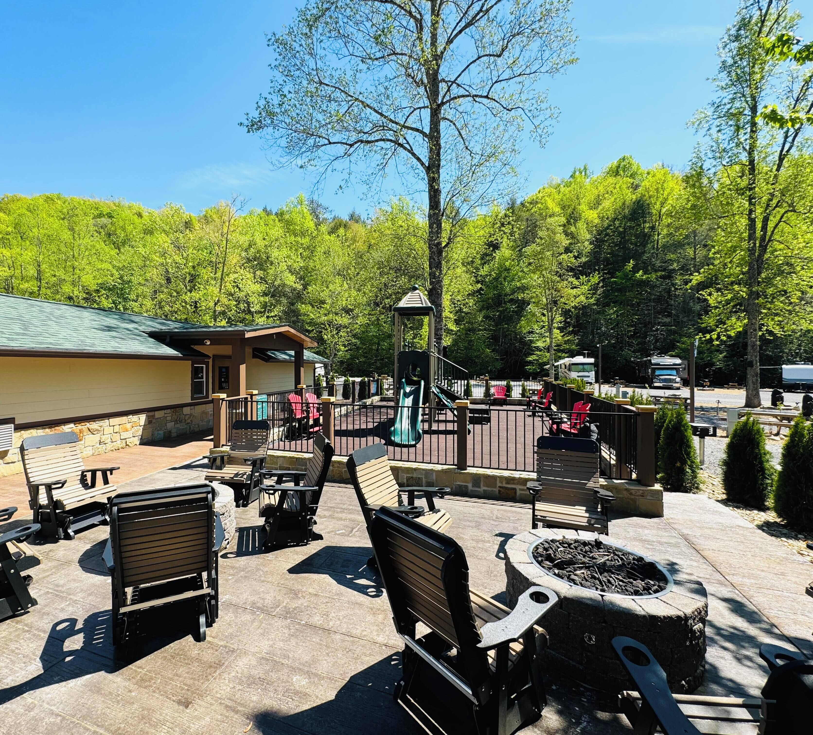 An outdoor patio area with seating and a fire pit, surrounded by trees and a building with a green roof.