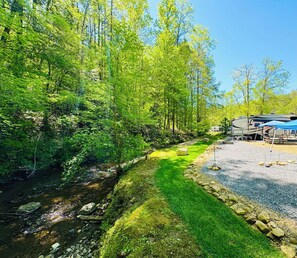 A campsite with RVs, a grassy area, and a stream. - Dudley Creek RV Resort (Gatlinburg)