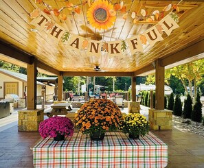 A covered outdoor area with a 'THANKFUL' banner, a checkered tablecloth, and potted flowers.
