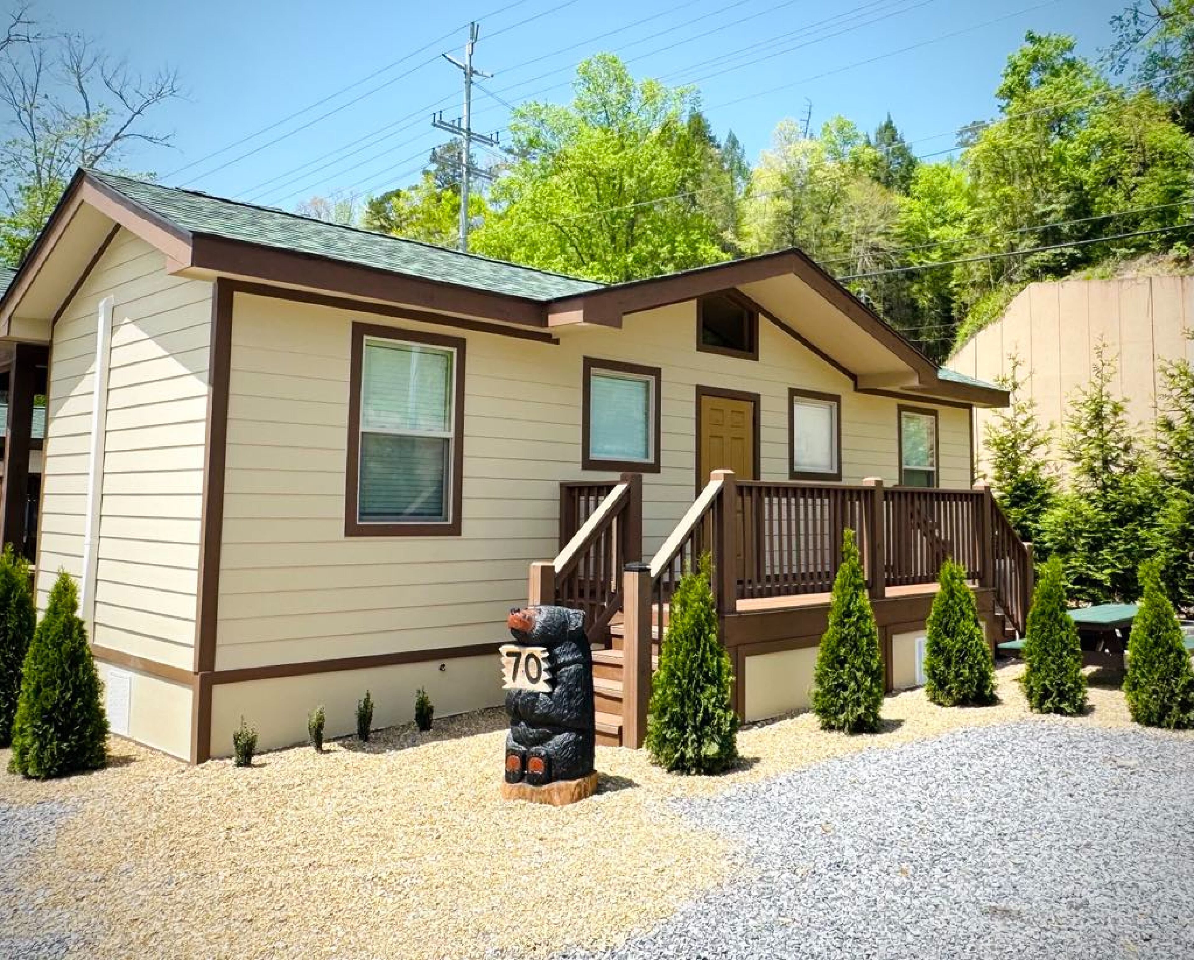 A single-story cabin with a front porch, a small deck, and a gravel driveway.