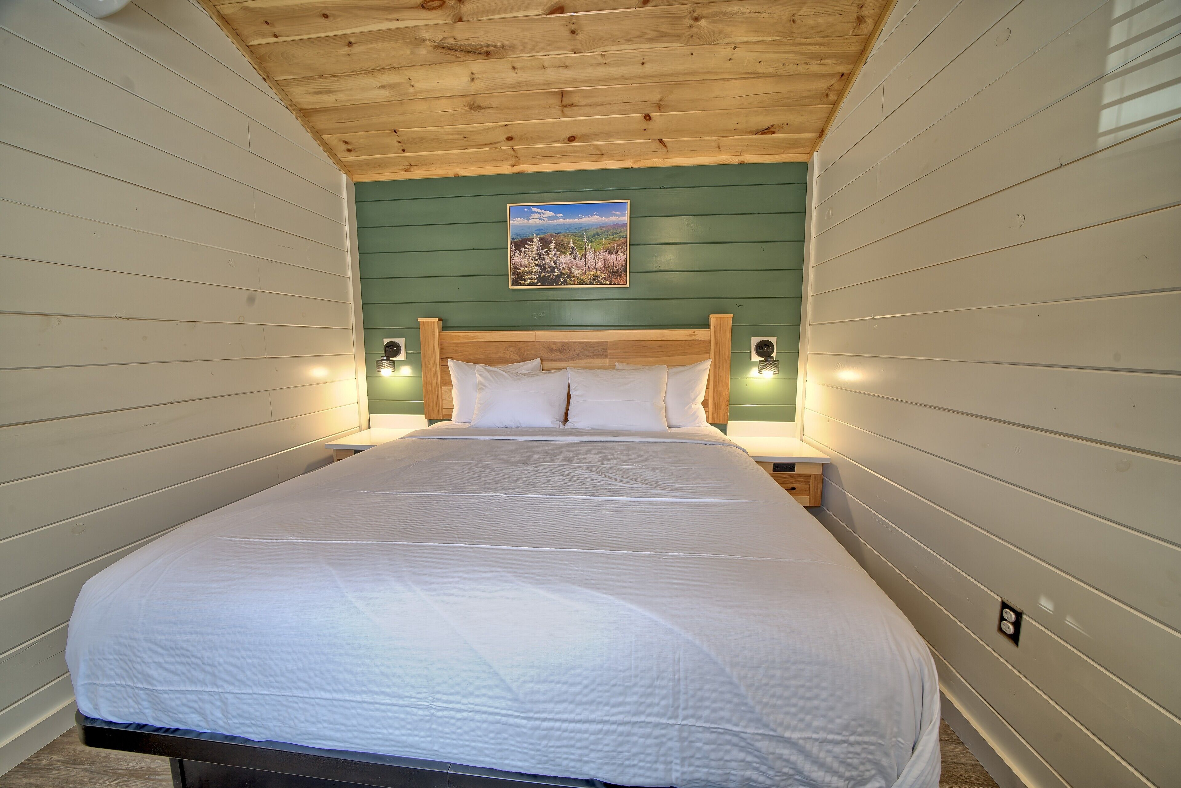 A bedroom with a wooden ceiling, green walls, a white bed, and two bedside lamps.