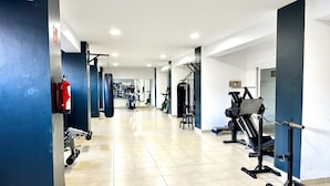 Uma academia com diversos equipamentos de ginástica, um extintor de incêndio e um espelho grande na parede.