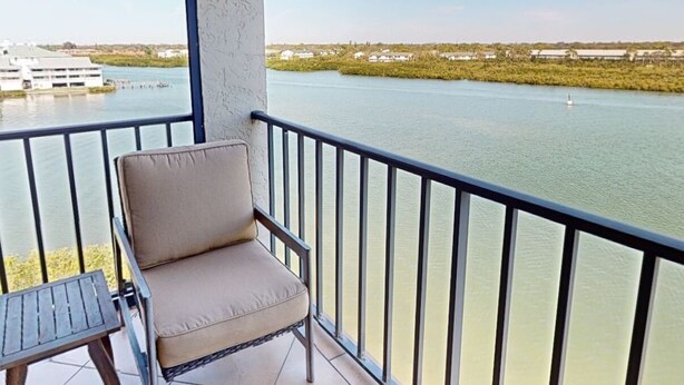 A balcony with a chair and a small table, overlooking a body of water with buildings in the distance.