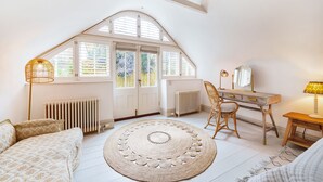Una habitación acogedora con techo inclinado, un ventanal grande, un escritorio de madera, una silla, un tapete redondo y un radiador.