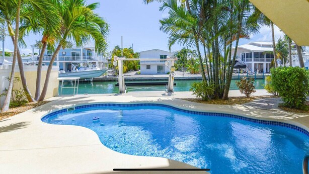 Una piscina de borde curvo, rodeada de palmeras y un muelle con barcos.
